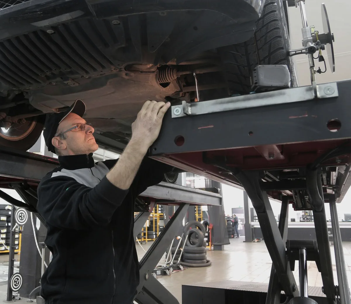 Mechanic inspecting the underside of a car raised on a hoist